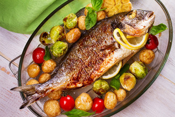 Roasted dorado fish with brussels sprouts, tomatoes, garlic, young potato and greens. View from above, top studio shot