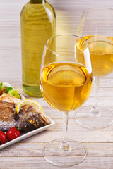 Glasses and bottle of white wine. Grilled dorado fish with vegetables in white plate