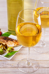Glasses and bottle of white wine. Grilled dorado fish with vegetables in white plate