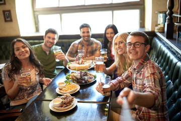 happy friends with selfie stick at bar or pub