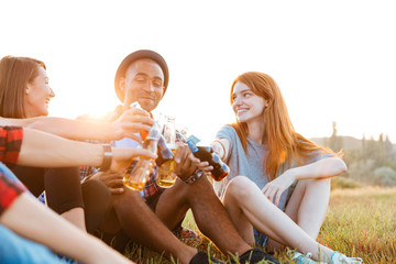 Group of happy young friends drinking beer and soda outdoors