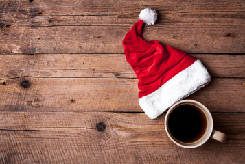 Obraz na płótnie Canvas Cup of coffee and Santas hat on a wooden background, celebration