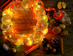 Christmas hand made craft template evening light background. Make traditional New Year`s door wreath components: tree cones, dried oranges, cinnamon, ribbon and colorful garland lights. Copyspace.