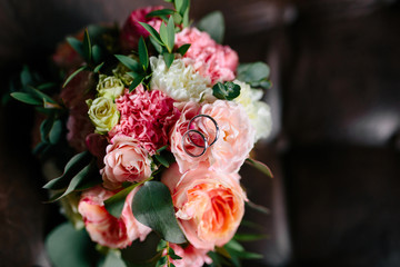 bouquet of pink flowers, white flowers and greenery on a brown background, wedding ring, silver coloured, the bouquet of peonies