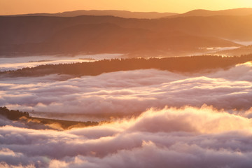 Summer weather phenomenon. Seasonal landscape with morning fog in valley. Clouds drenched valley below the level of the mountains. Sunrise over creeping clouds.