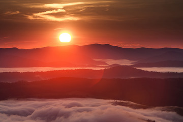 Summer weather phenomenon. Seasonal landscape with morning fog in valley. Clouds drenched valley below the level of the mountains. Sunrise over creeping clouds.