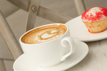 cup of coffee with saucer and cake on the table against the background of the chair