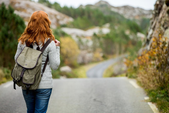 Woman traveler with a backpack on his shoulders walking along the road. The road through the rocks. Scandinavia, autumn, cloudy.
