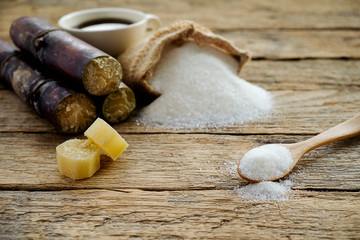 Sugar in wooden spoon with sugar in burlap sack, sugarcane on wooden desk. Sugar crystals closeup. Soft focus(selective focus).