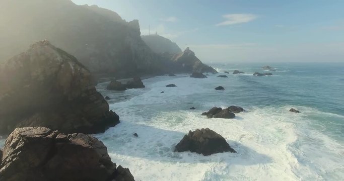 Beautiful aerial or drone shot along the coast of Portugal on a sunny day. Epic cliffs and ocean waves birds eye view during sunrise. Untouched, powerful nature. Cabo da Roca, Portugal Europe.