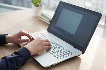 Hands typing on a laptop keyboard. A man works in an office at his workplace