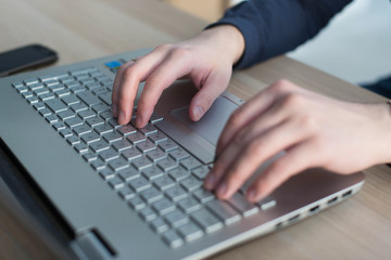 Hands typing on a laptop keyboard. A man works in an office at his workplace