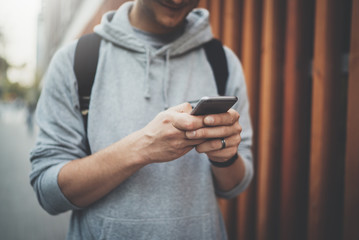 Close-up image of male hands using modern smartphone device outdoor, young hipster guy reading information in internet while going to work, technology and social networking concept