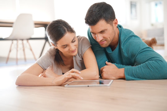 Couple connected on digital tablet, laying on floor