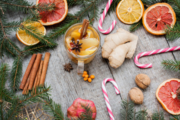 Christmas composition. Spruce branches, candy cane, warming tea with ginger and lemon,  dried oranges, grapefruit, cinnamon, star anise, pomegranates on a wooden background.