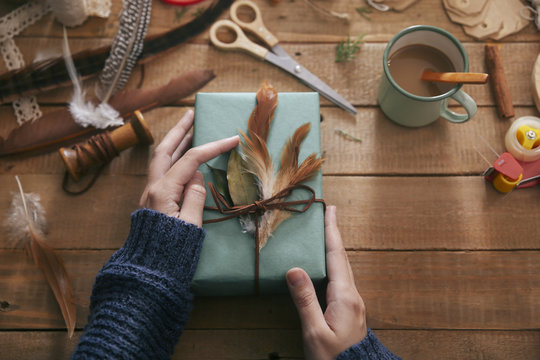 Woman decorating Christmas present with leaf and feathers, close-up