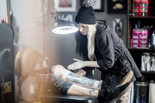 Female tattoo artist applying protective wrap on finished tattoo