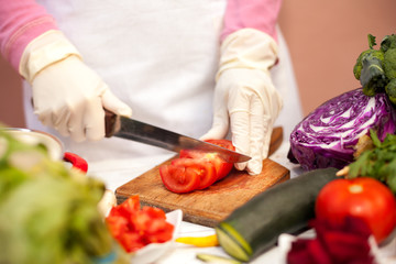 Woman with glove cutting tomato in the kitchen