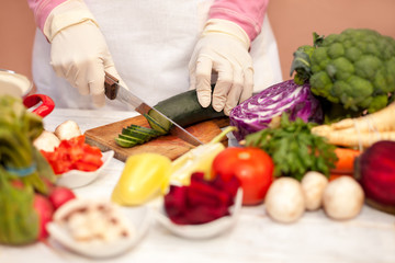 Housewife with white glove slicing cucumber with a knife