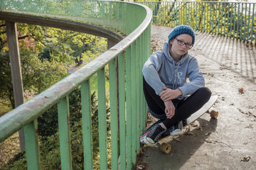 Girl sitting on skateboard on urban autumn modern retro grunge ramp, looking at camera