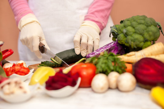 Housewife with white glove slicing cucumber and preparing vegeta