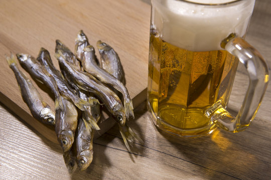Beer and dried fish on wooden table.