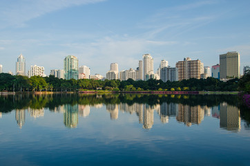 the skyline of metropolis building with the green park and blue sky background , the city park reflection from water in lake.