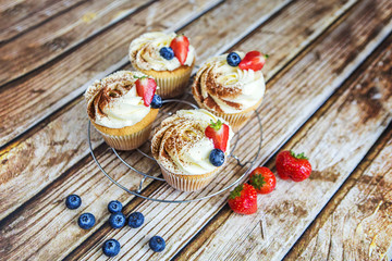 Пирожные с кремом, посыпанным какао, и ягодами клубники и голубики на железной решетке на деревянном столе.