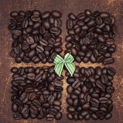 Small green bow on dark roasted coffee beans divided into quarters on a faux leather material background