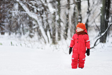 Fototapeta na wymiar Portrait of little funny boy in red winter clothes having fun with snow during snowfall