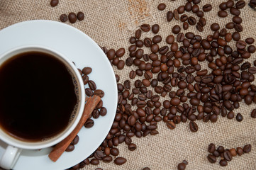 Coffee beans and white cup with cinnamon sticks on sackcloth
