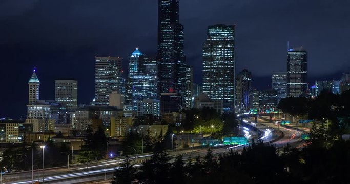 Seattle, Washington, USA - illuminated skyline of Seattle as seen from Dr. Jose Rizal Park with Interstate 5 at night with moving clouds - Timelapse with zoom out