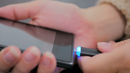 Woman's hand plugging black lightning charging cable into smartphone - USB data cable connecting on modern gadget. Close up