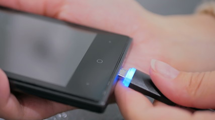 Woman's hand plugging black lightning charging cable into smartphone - USB data cable connecting on modern gadget. Close up