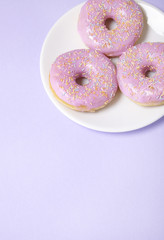 A plate of ring donuts with pastel pink frosting and sprinkles on a purple background with blank space below