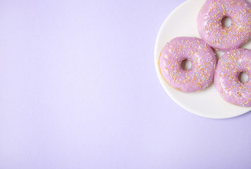 A plate of ring donuts with pastel pink frosting and sprinkles on a purple background with empty space at side