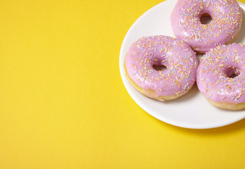 A plate of ring donuts with pastel pink frosting and sprinkles on a bright yellow background with empty space at side