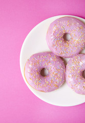 A plate of ring donuts with pastel pink frosting and sprinkles on a colorful background
