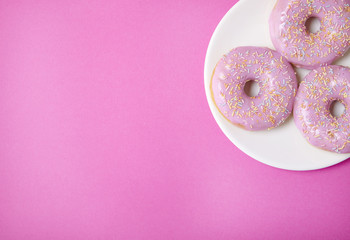 A plate of ring donuts with pastel pink frosting and sprinkles on a colorful background with blank space at side
