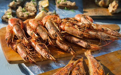 Grilled shrimp or prawn on the table. Shrimps on the wooden cutting board, surrounded by other sea delicacies.