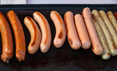 Different kinds of sausages are fried on the stove. Sausages are cooking for a party