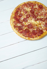 A whole, cooked and sliced peperoni pizza on a painted wooden table top background with blank space below