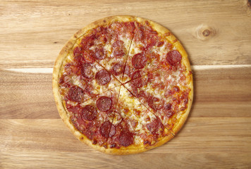 A whole, cooked and sliced peperoni pizza on a wooden kitchen counter top background