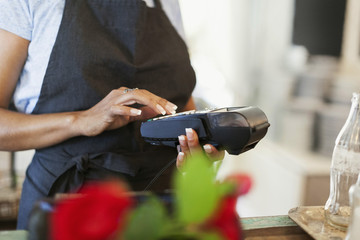 Midsection of female owner using credit card reader at cafe