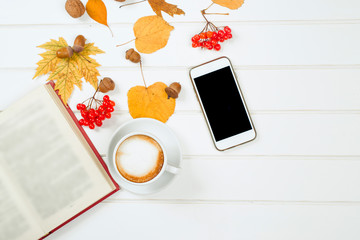 Cup of cappuccino near mobile phone on autumn background. Top vi