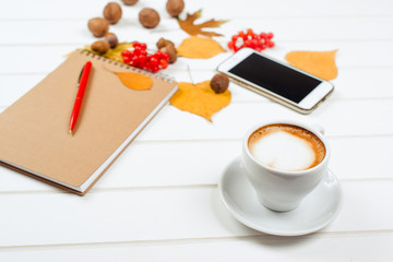Autumn background, notebook with pen, cup of cappuccino near mobile phone on wooden table.