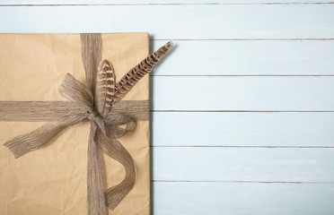 A gift wrapped in brown paper with rustic bow, on a painted wooden table background with blank...