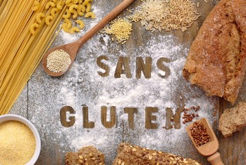 Gluten free flour and cereals millet, quinoa, corn flour polenta, brown buckwheat, basmati rice and pasta with text gluten free in French language with wooden spoon on brown wooden background © luciepeclova