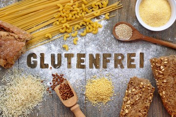 Gluten free flour and cereals millet, quinoa, corn flour polenta, brown buckwheat, basmati rice and pasta with text gluten free in German language with wooden spoon on brown wooden background © luciepeclova