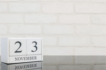 Closeup white wooden calendar with black 23 november word on black glass table and white brick wall textured background with copy space , selective focus at the calendar